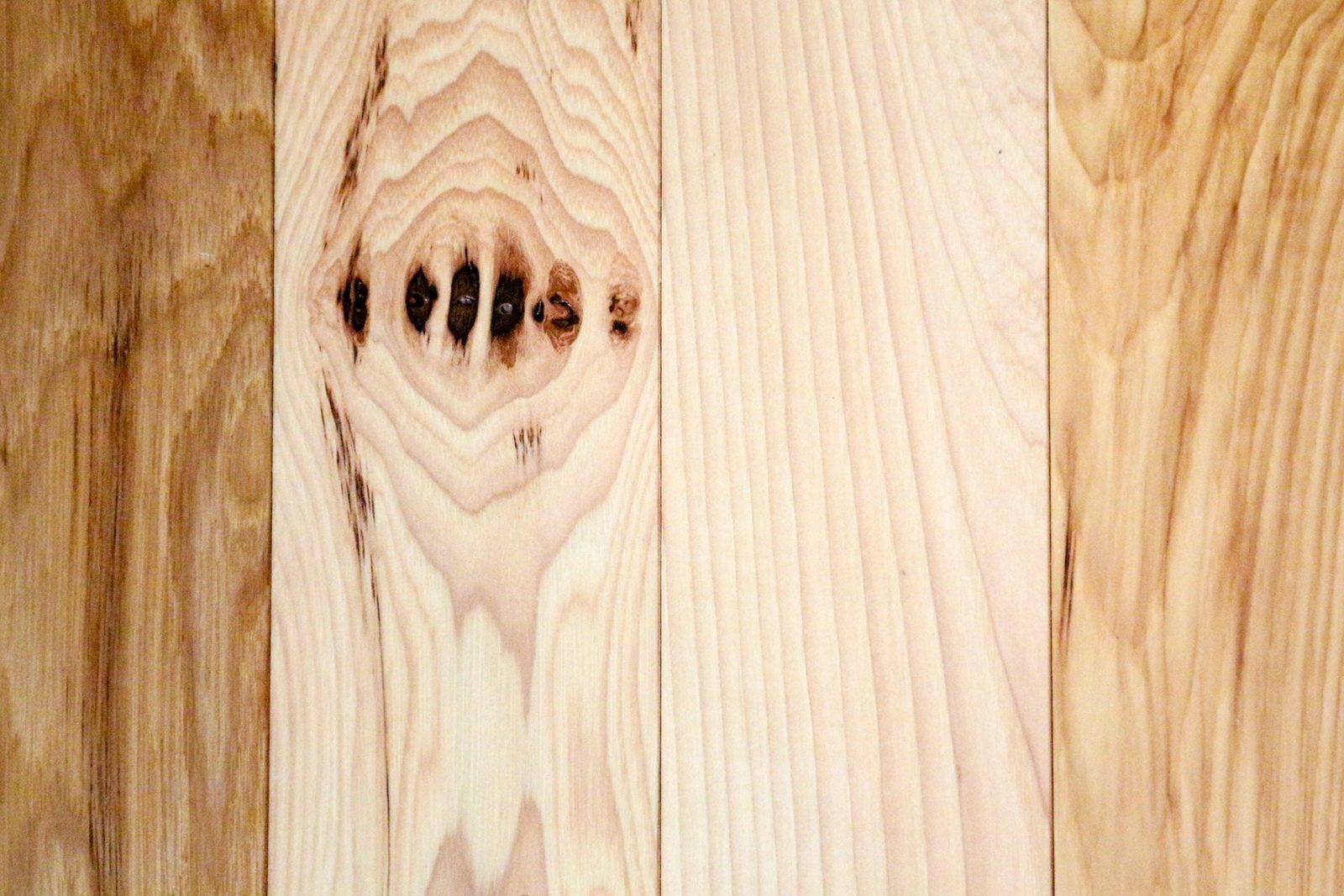 Three wooden plank sections display varying grain patterns and colors, showcasing natural textures and slight imperfections in a light, neut