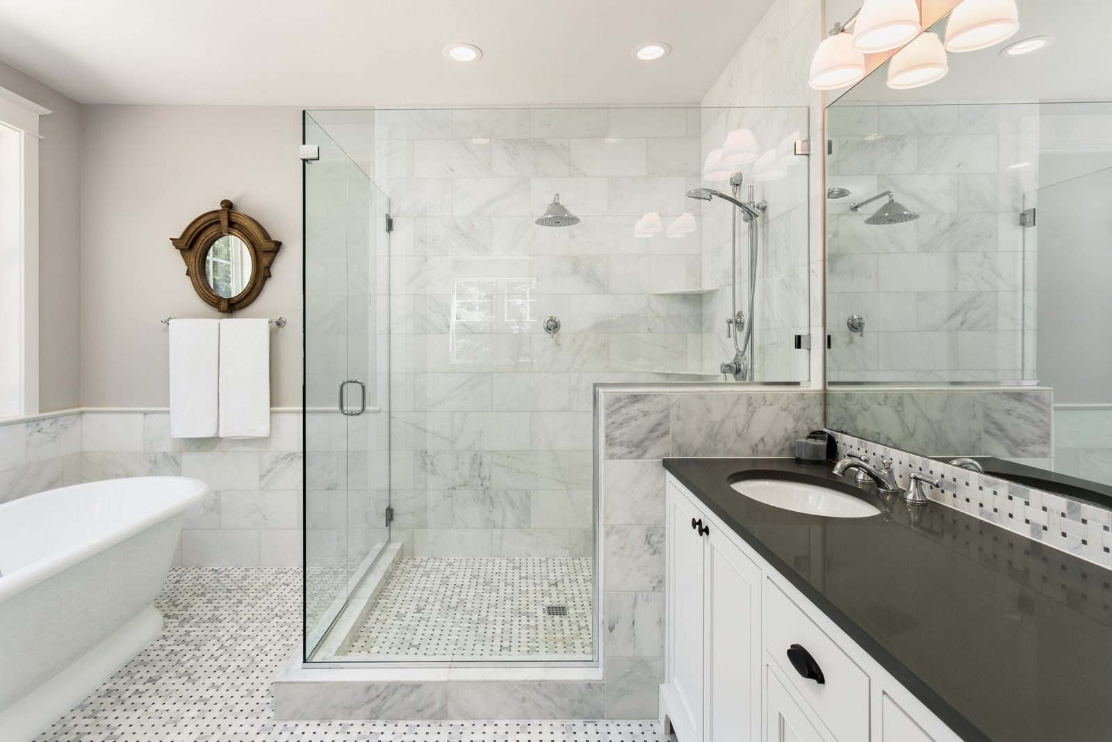 A modern bathroom features a glass shower and freestanding tub, with marble walls and patterned flooring, complemented by a decorative mirro