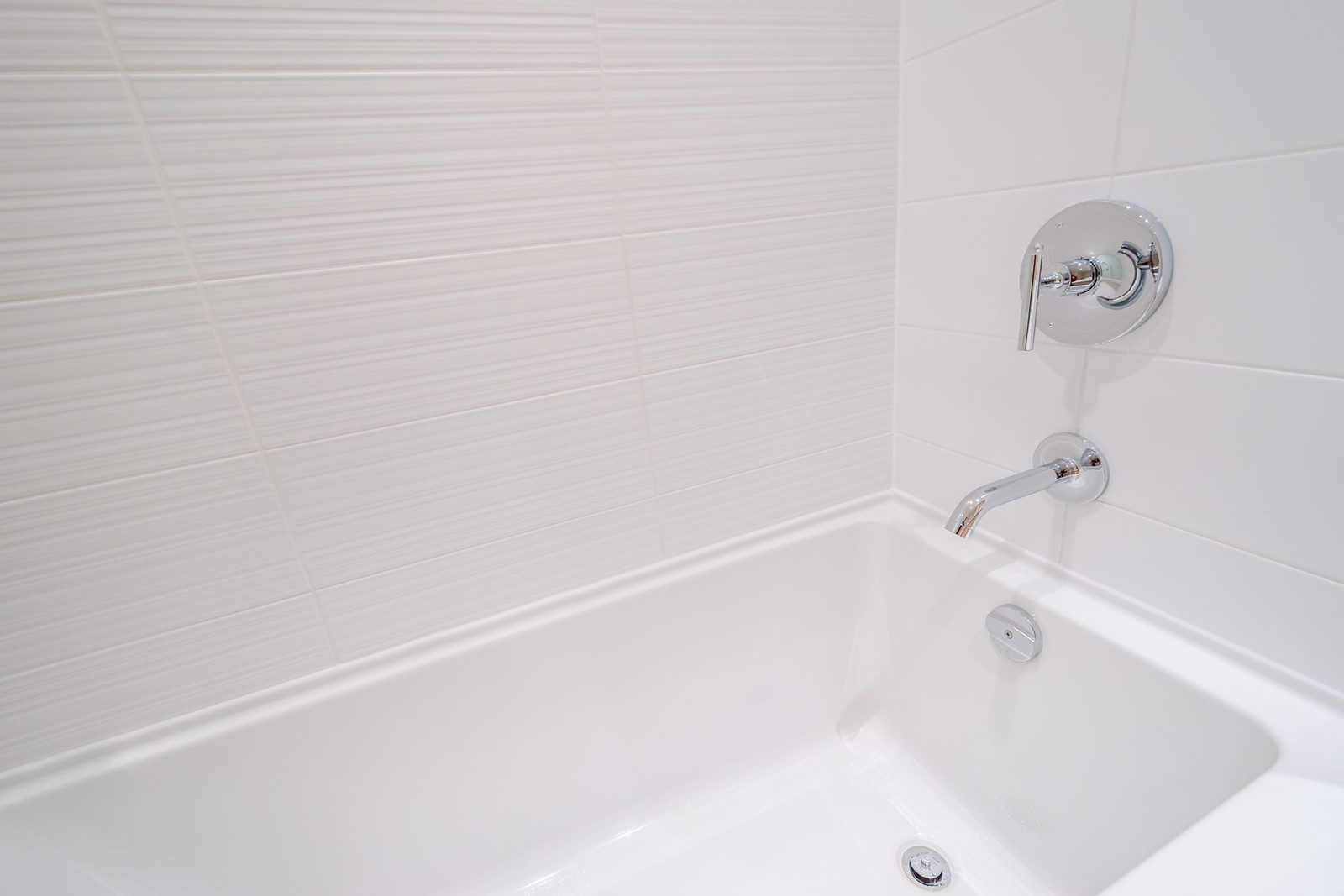 A white bathtub with a chrome faucet is positioned against a subtle textured wall, reflecting a clean and modern bathroom aesthetic.
