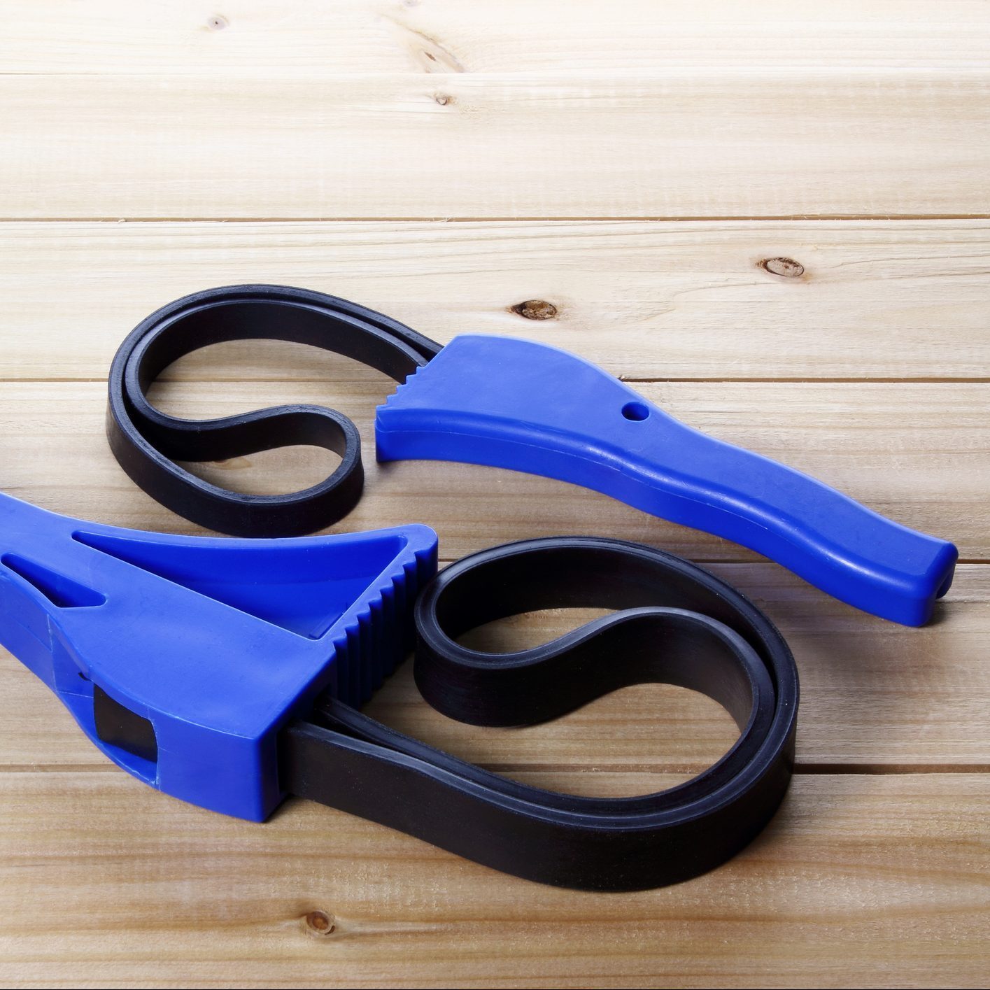 Two blue and black rubber tools lay on a wooden surface, designed for gripping or opening containers, showcasing curved and straight compone