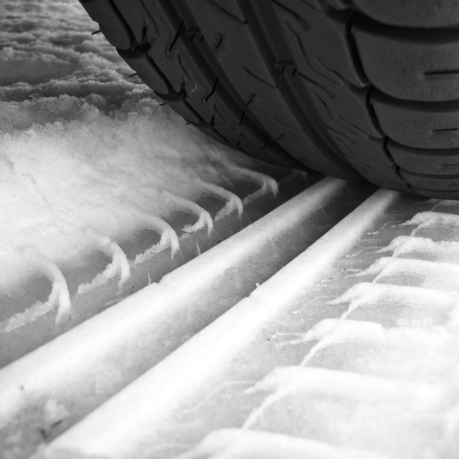 A tire presses down into snow, leaving distinct tracks in the white surface, indicating movement on a wintery ground.