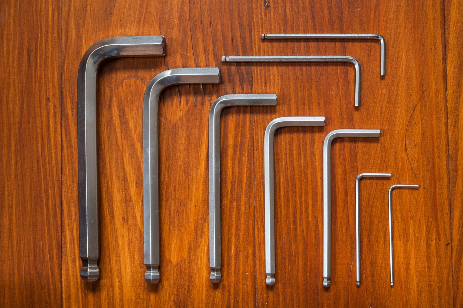 Several metal Allen wrenches of varying sizes are arranged on a wooden surface, showcasing their straight and L-shaped designs.