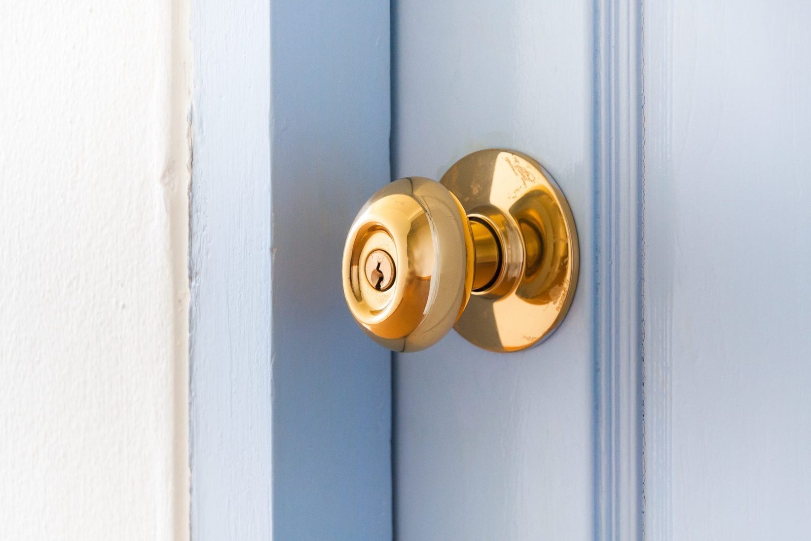 A shiny gold doorknob is positioned on a light blue door, suggesting potential entry or exit in a well-lit, indoor setting.