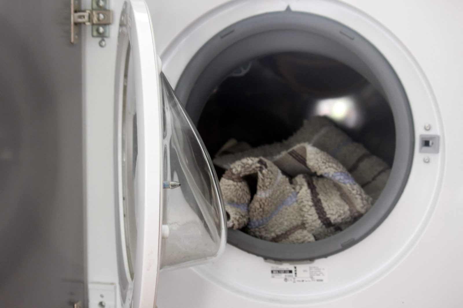 A washing machine door is open, revealing a striped towel inside, ready for a wash cycle in a clean, well-lit laundry space.