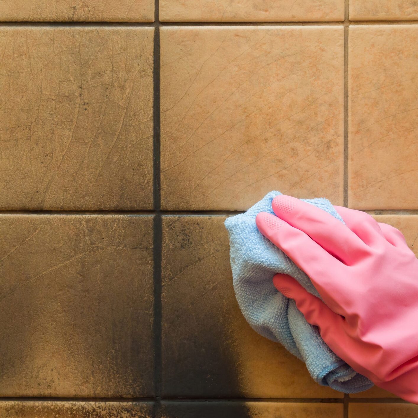 hand in rubber protective glove with rag washing black soot marks from beige wall tiles