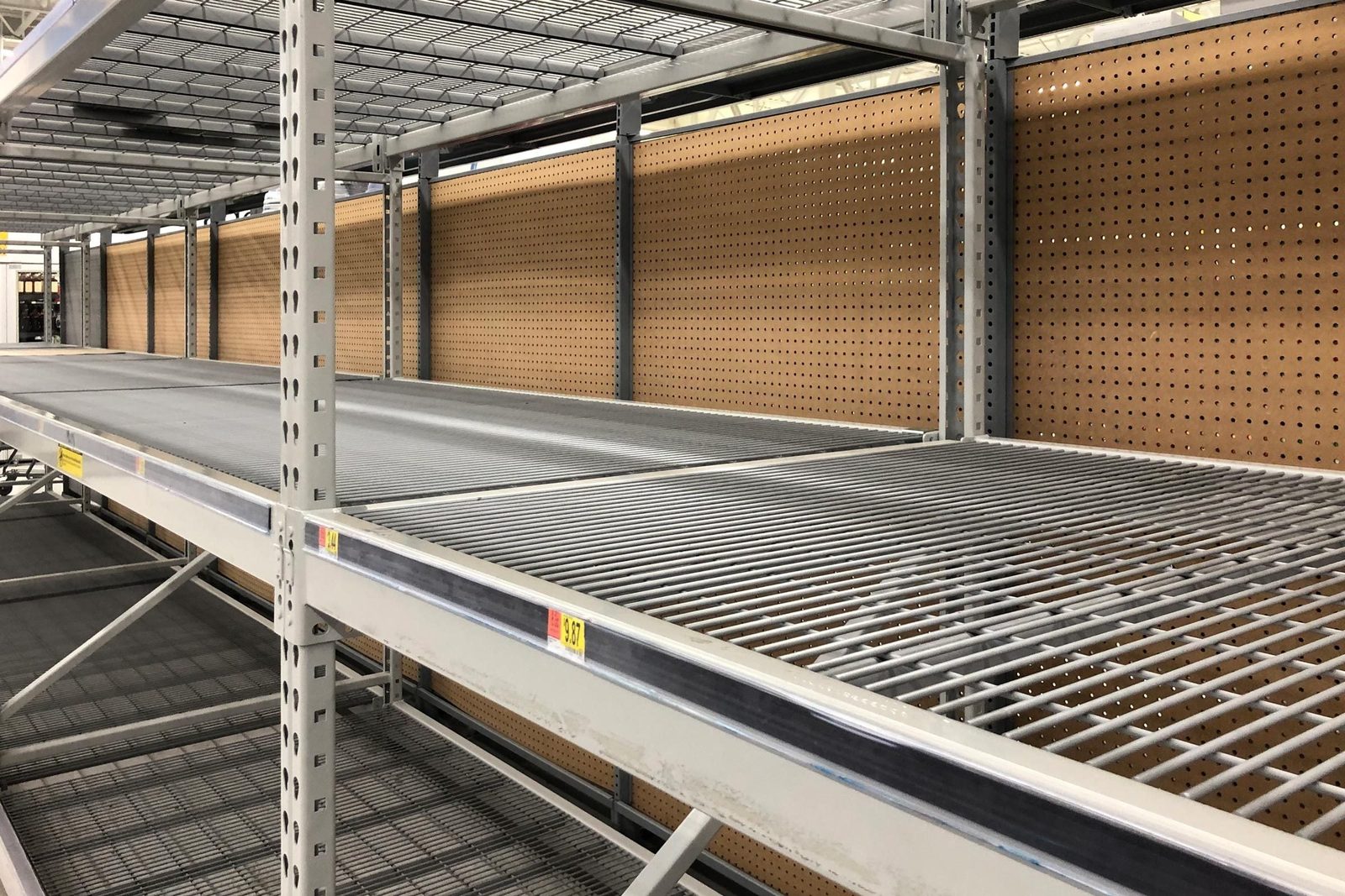 Metal shelving units stand empty in a store, with a plain, perforated wall behind them, indicating a lack of displayed products.