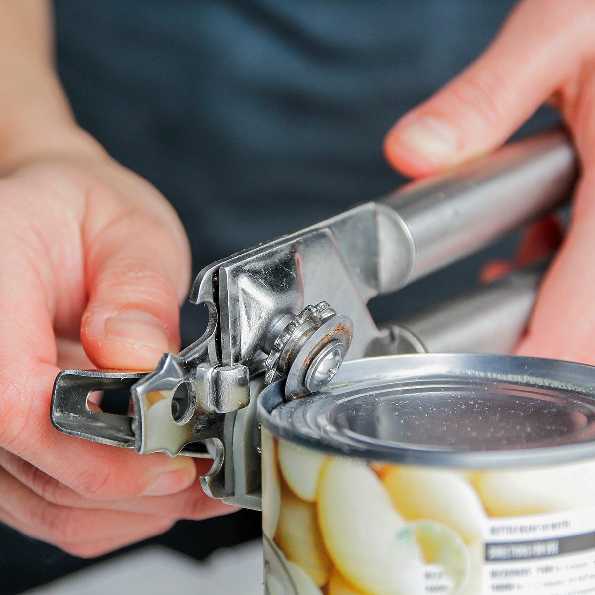 Closeup of hands opening a can using can opener