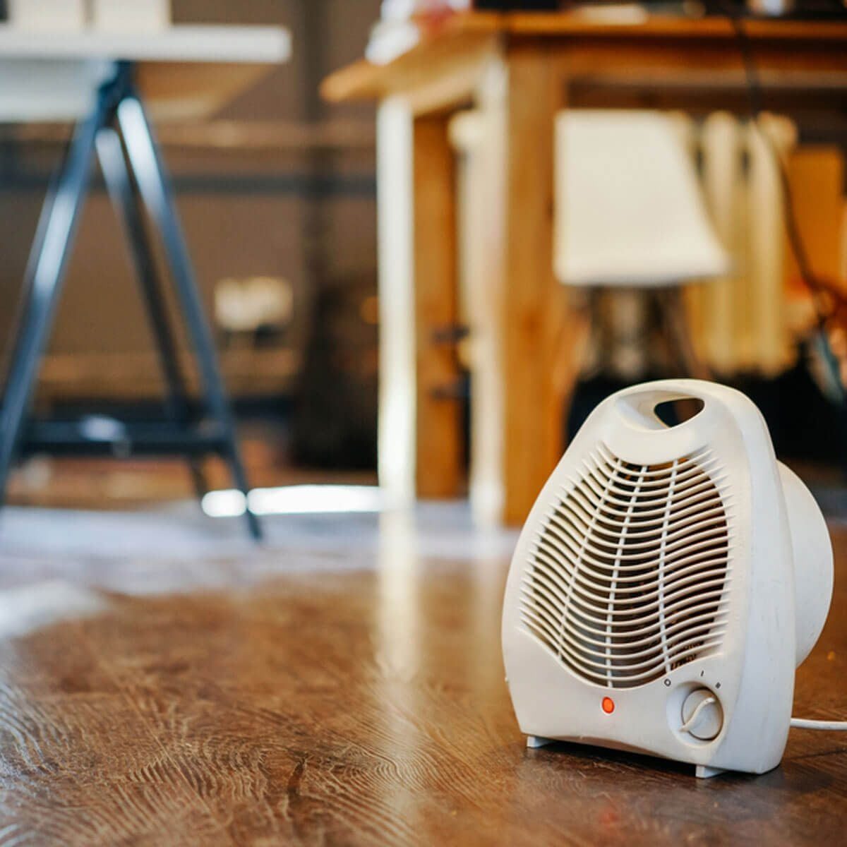 A white space heater sits on a wooden floor, providing warmth in a well-lit room with furniture in the background.