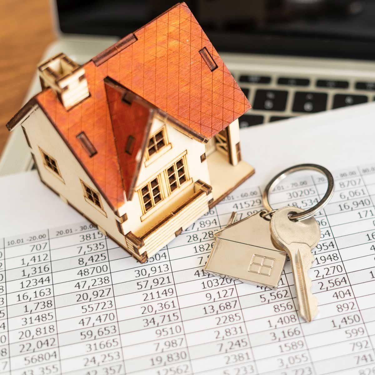 A miniature house sits on financial documents with keys attached to a keyring nearby, suggesting a focus on real estate transactions or inve