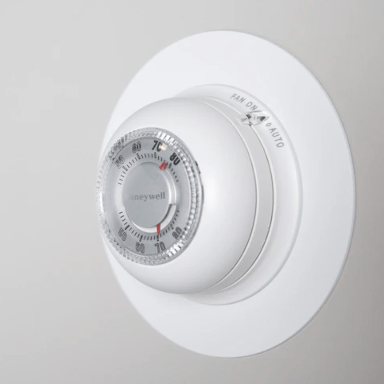 A round thermostat displays temperature settings and options. It is mounted on a smooth, light-colored wall, indicating functionality for cl