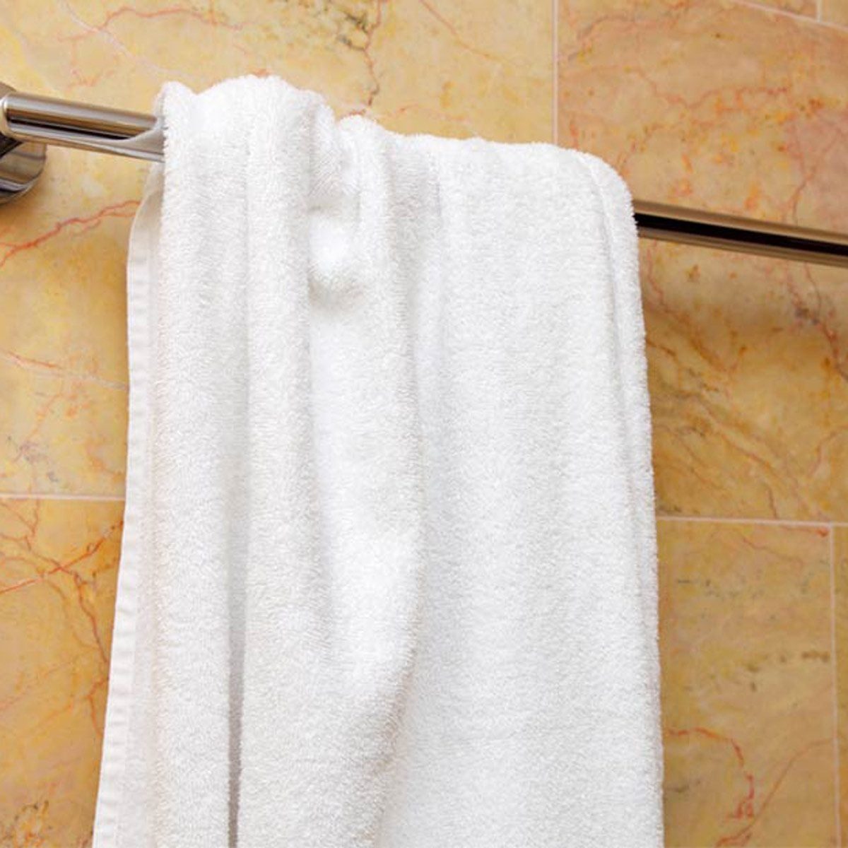 A white towel hangs on a silver rod against a textured, light-colored tiled wall, suggesting a bathroom environment.