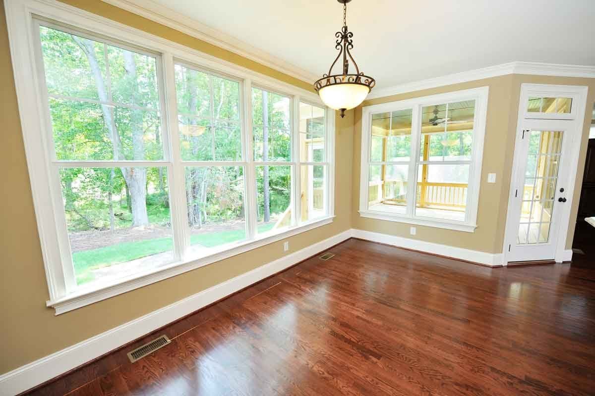 A bright room features large windows showcasing a green landscape, while a pendant light hangs from the ceiling and hardwood floors provide