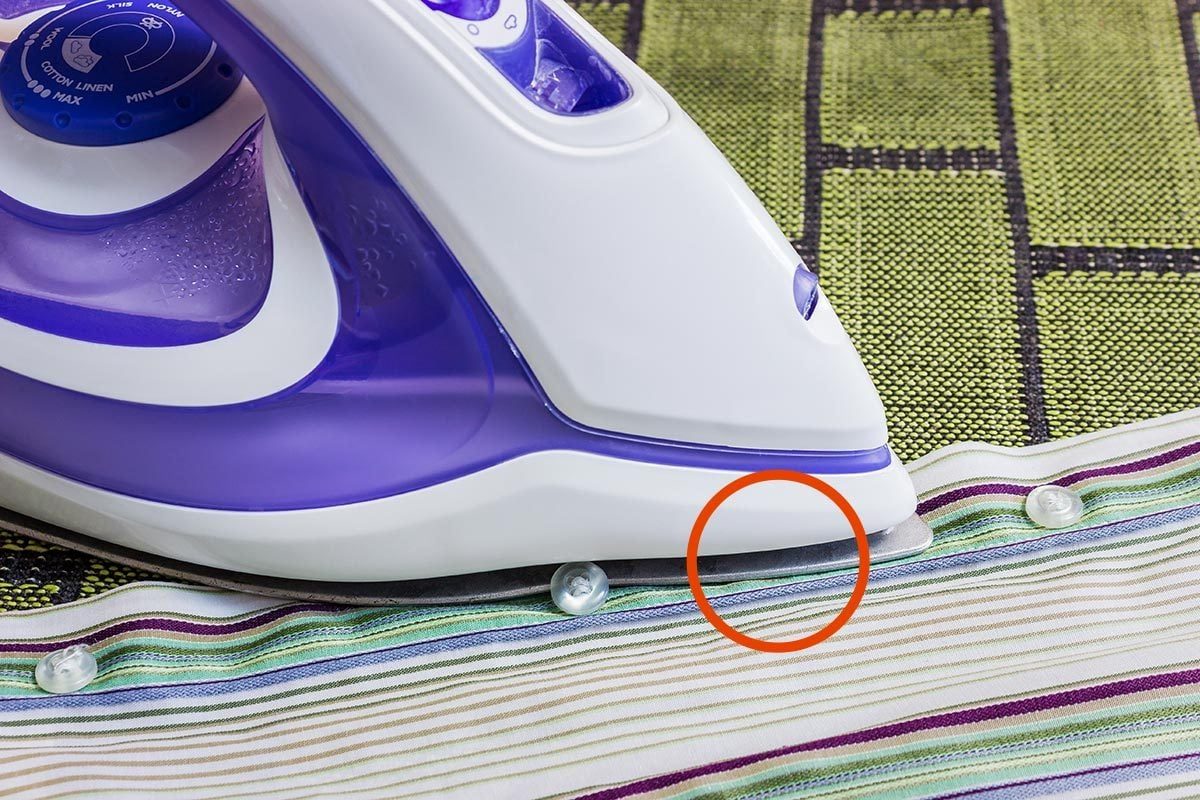 Purple and white iron with a groove between the plastic body and the metal iron plate, with a red circle around a section of the groove, on