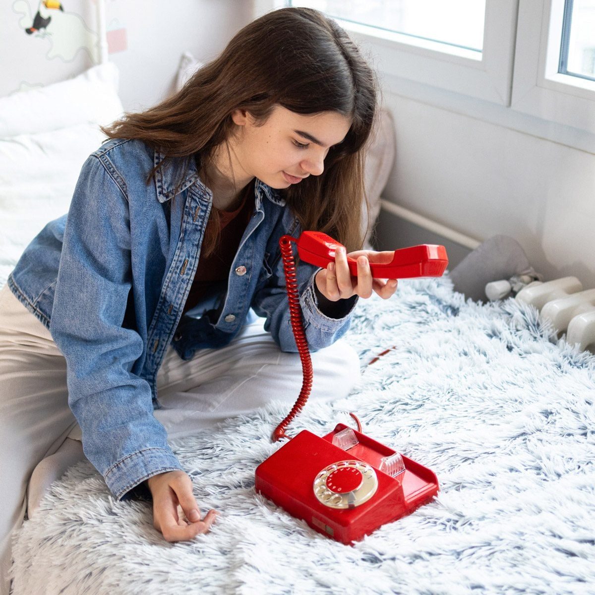 young girl on her bed holding an old rotary phone
