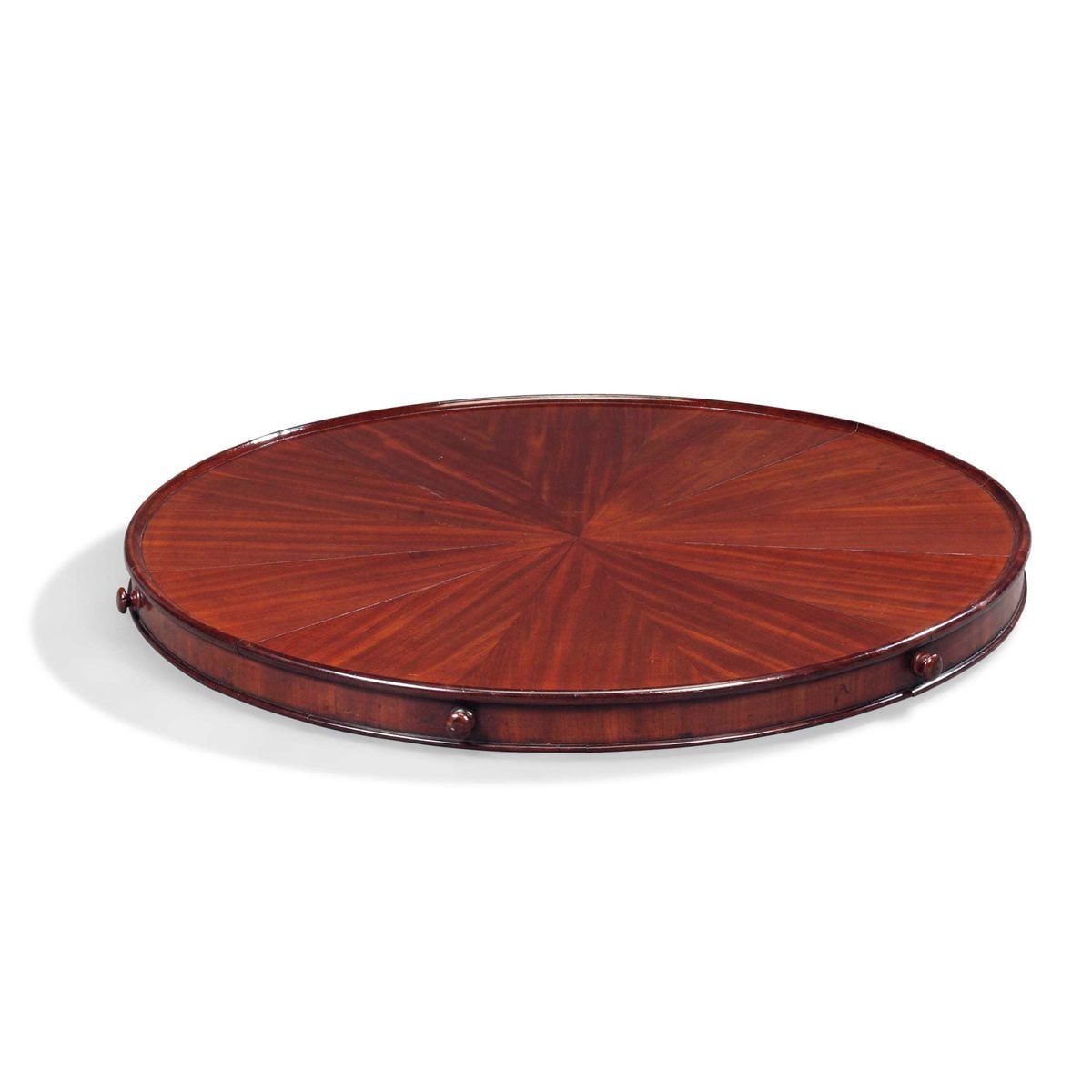 A round wooden tray rests on a flat surface, featuring a sunburst pattern; its deep brown finish highlights its polished texture.