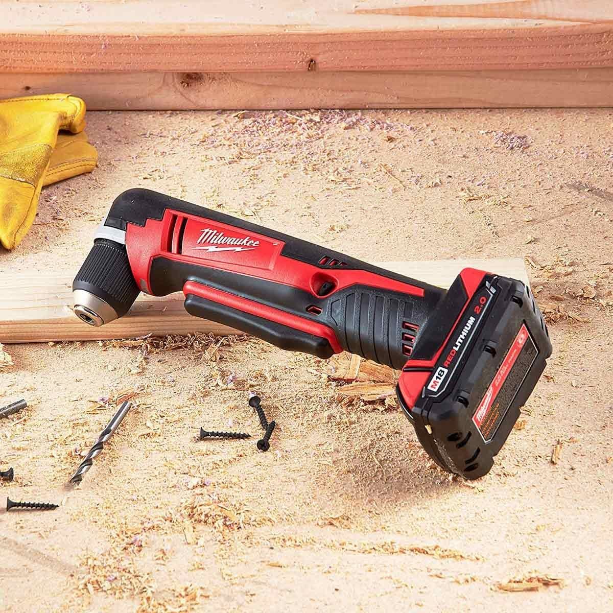 A cordless power tool rests on a wooden surface, surrounded by wood shavings, screws, and a yellow glove, indicating a construction or craft