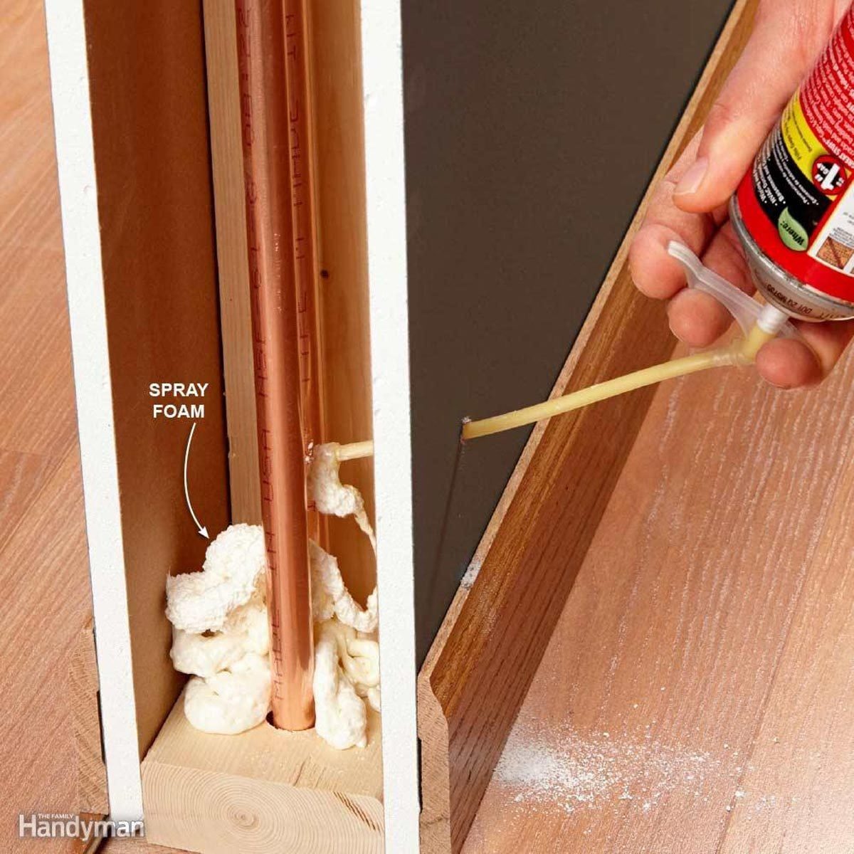 A hand sprays foam insulation into a gap around copper pipes within a wooden structure, enhancing energy efficiency in a home setting.