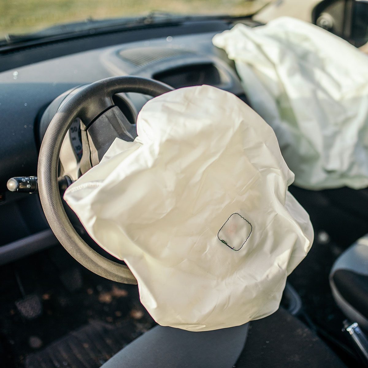 Car crashed in an accident on a highway or city street. Broken glass is all around and the airbag is ope
