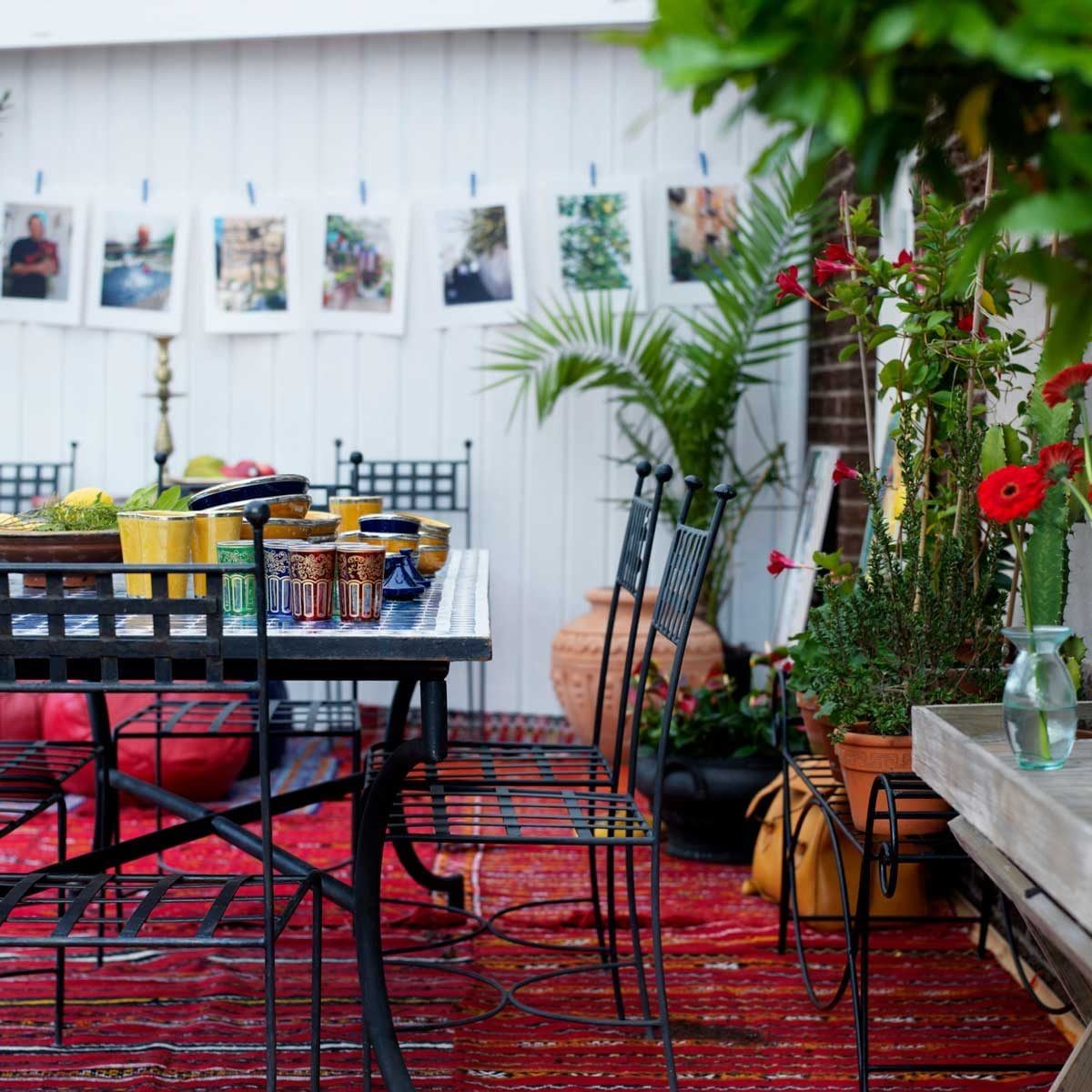A dining table is adorned with colorful dishes and drinks, surrounded by chairs, greenery, and decorative photos against a white wall in an