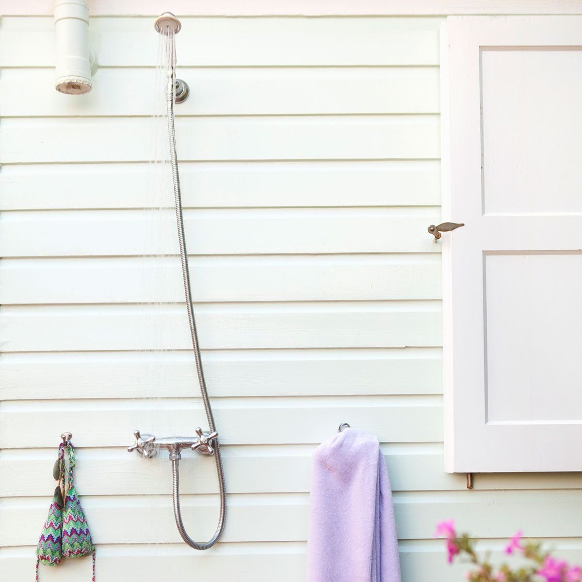 A showerhead sprays water downwards, mounted on a light green wooden wall, accompanied by a purple towel and decorated with hanging items.