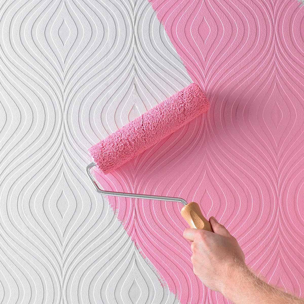 A paint roller applies pink paint to a textured white wall, covering half of the surface with smooth, flowing patterns against a light backg