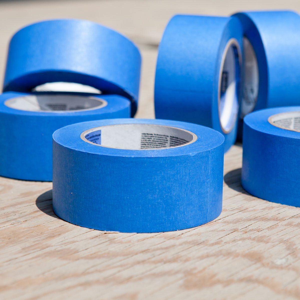 Five rolls of blue masking tape rest on a wooden surface, showcasing their smooth texture and circular shape in natural light.