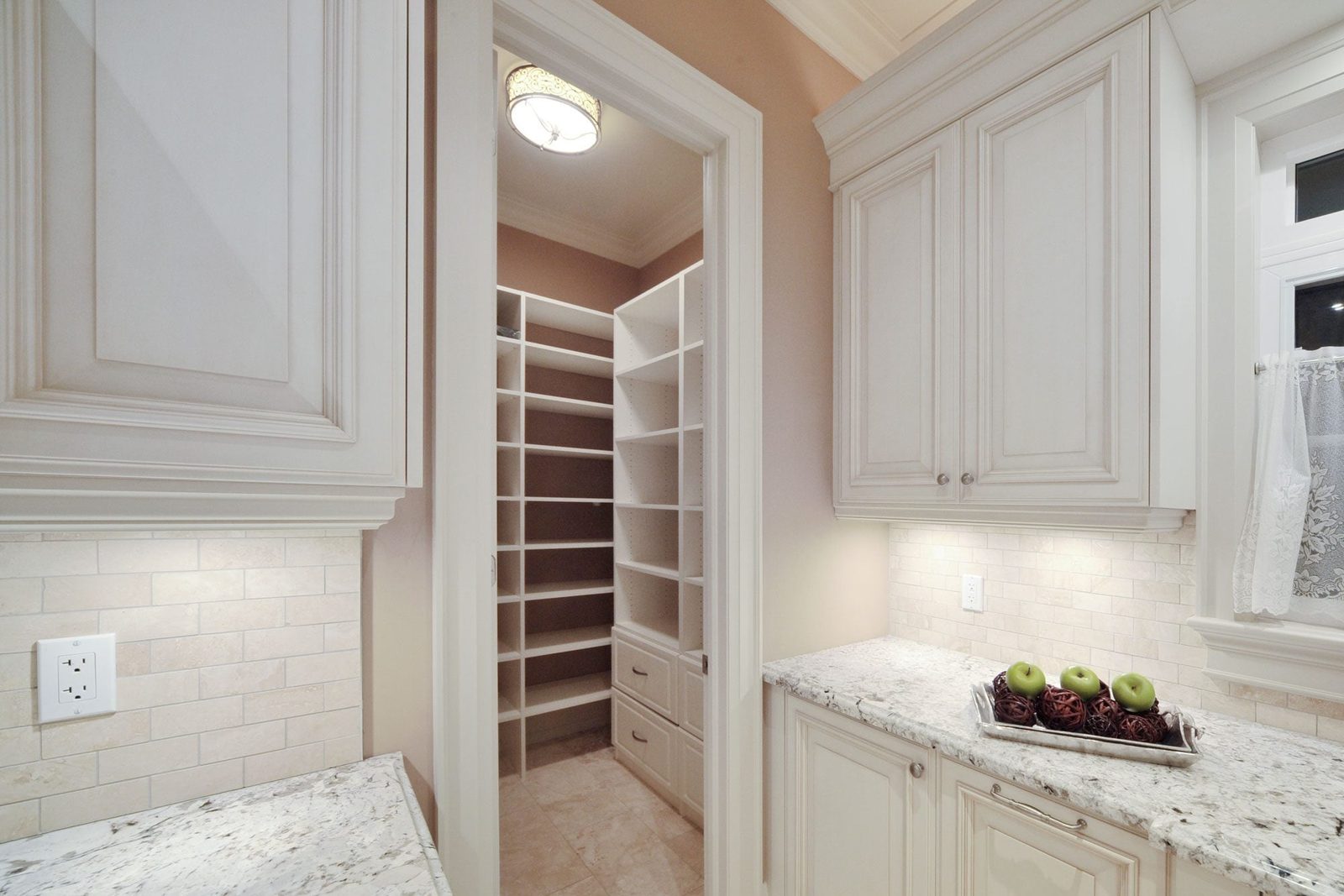 A pantry door opens to reveal shelves, while a kitchen countertop displays a decorative tray with green apples and decorative items in a sof