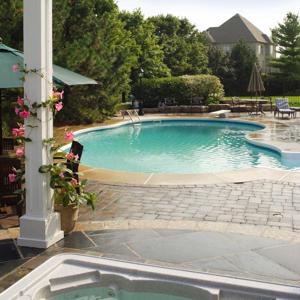 A swimming pool glistens under sunlight, surrounded by greenery and lounge chairs, with pink blooming flowers climbing a white pillar nearby