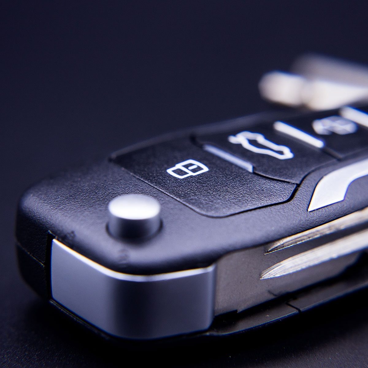 A car key fob rests on a dark surface, displaying buttons for unlocking, opening the trunk, and a mechanical key blade.