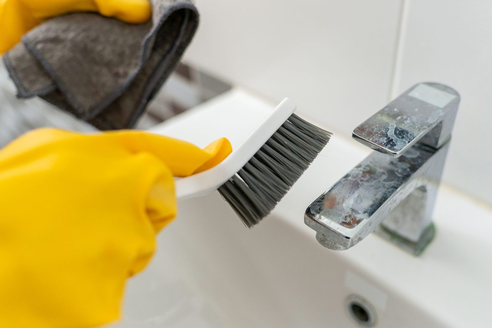 Close up of woman hands with gloves holding brush cleaning bathroom faucet to remove limescale