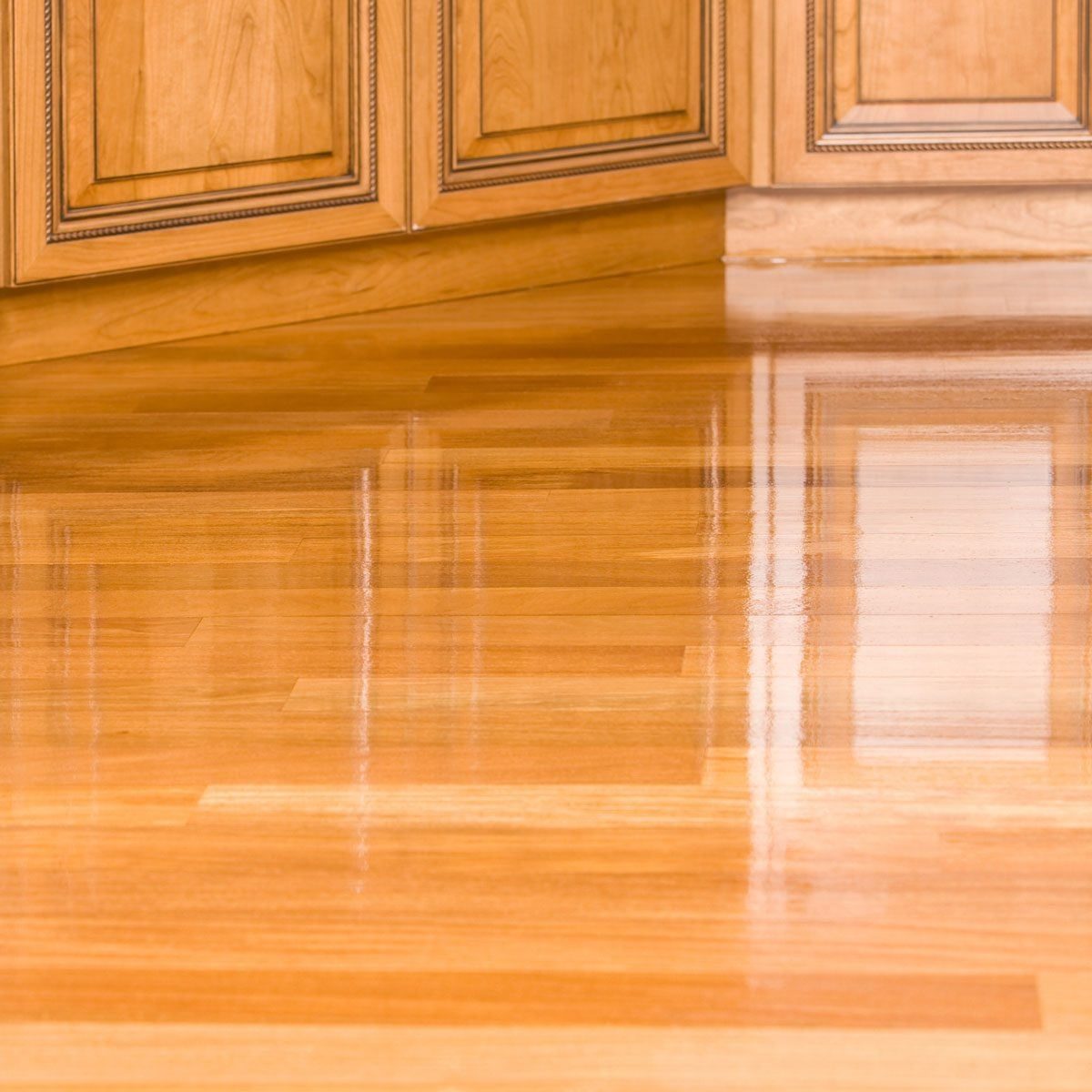 Polished hardwood flooring reflects light, showing a smooth surface. It meets wooden cabinetry at a corner, creating a warm, inviting interi