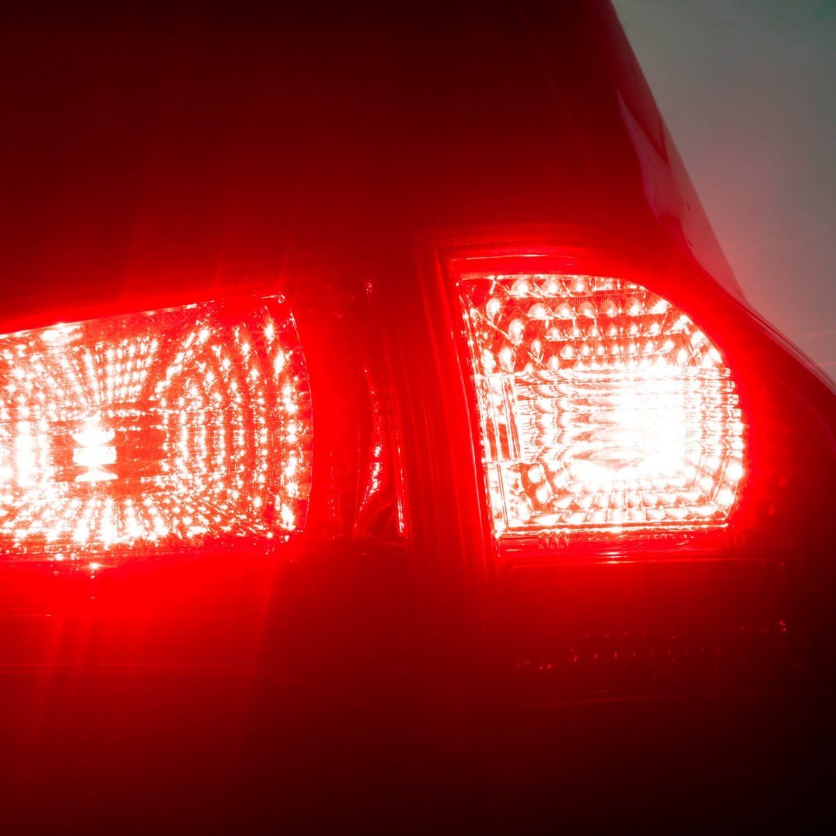 A car’s red taillights illuminate brightly, indicating braking. The dark background emphasizes their vivid glow, suggesting nighttime or dim