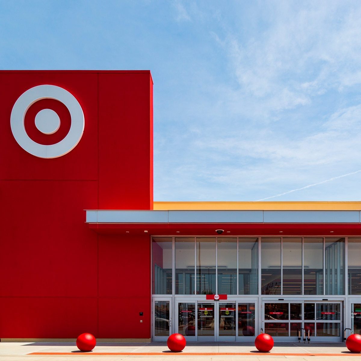 A large, red building featuring a circular logo stands prominently against a clear sky, with round red balls placed in front of the entrance