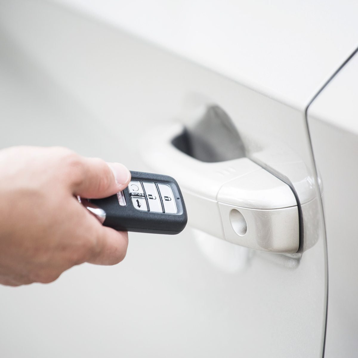 A hand holds a car key fob, pressing a button near a silver car's door handle, indicating an attempt to unlock the vehicle.