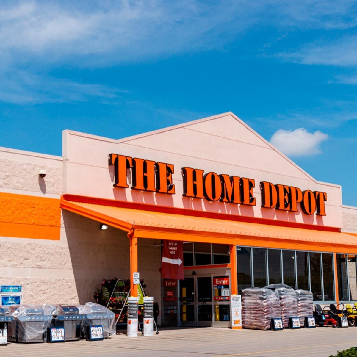 A large retail store displays "THE HOME DEPOT" in bold orange letters, with shopping carts and outdoor products outside, set against a clear