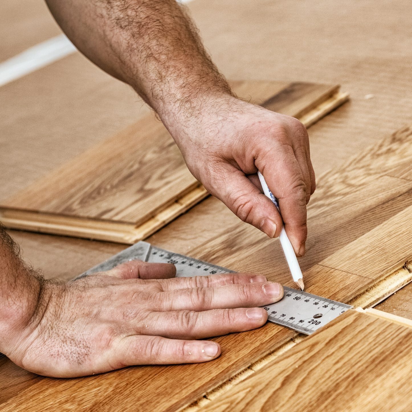 A hand uses a ruler and pencil to mark measurements on wooden planks on a work surface, focused on precision in a carpentry setting.