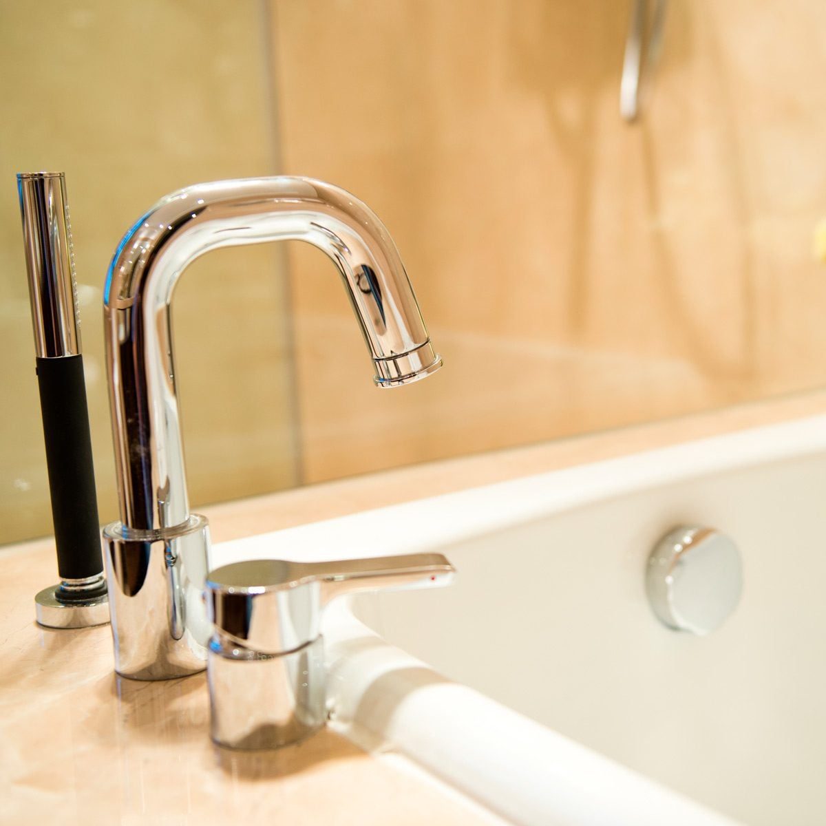 A chrome faucet is positioned above a bathtub, with water possibly flowing. The background features light-colored walls, creating a warm, in