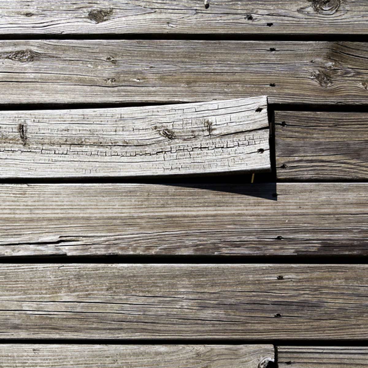A wooden plank, slightly elevated, rests unevenly against a series of flat, parallel wooden boards, creating a textured surface in natural l