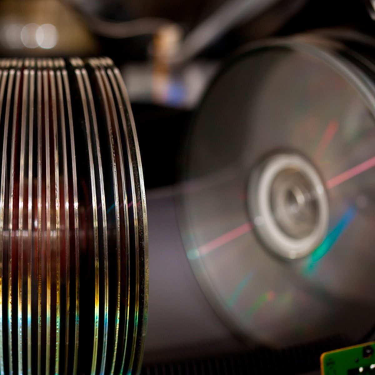 A stack of shiny optical discs and a partially visible metallic cylinder rotate against a dark backdrop, evoking a sense of movement in a te