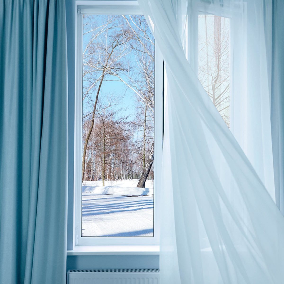 A window displays a snowy landscape with bare trees under a clear blue sky, partially covered by sheer curtains blowing gently.