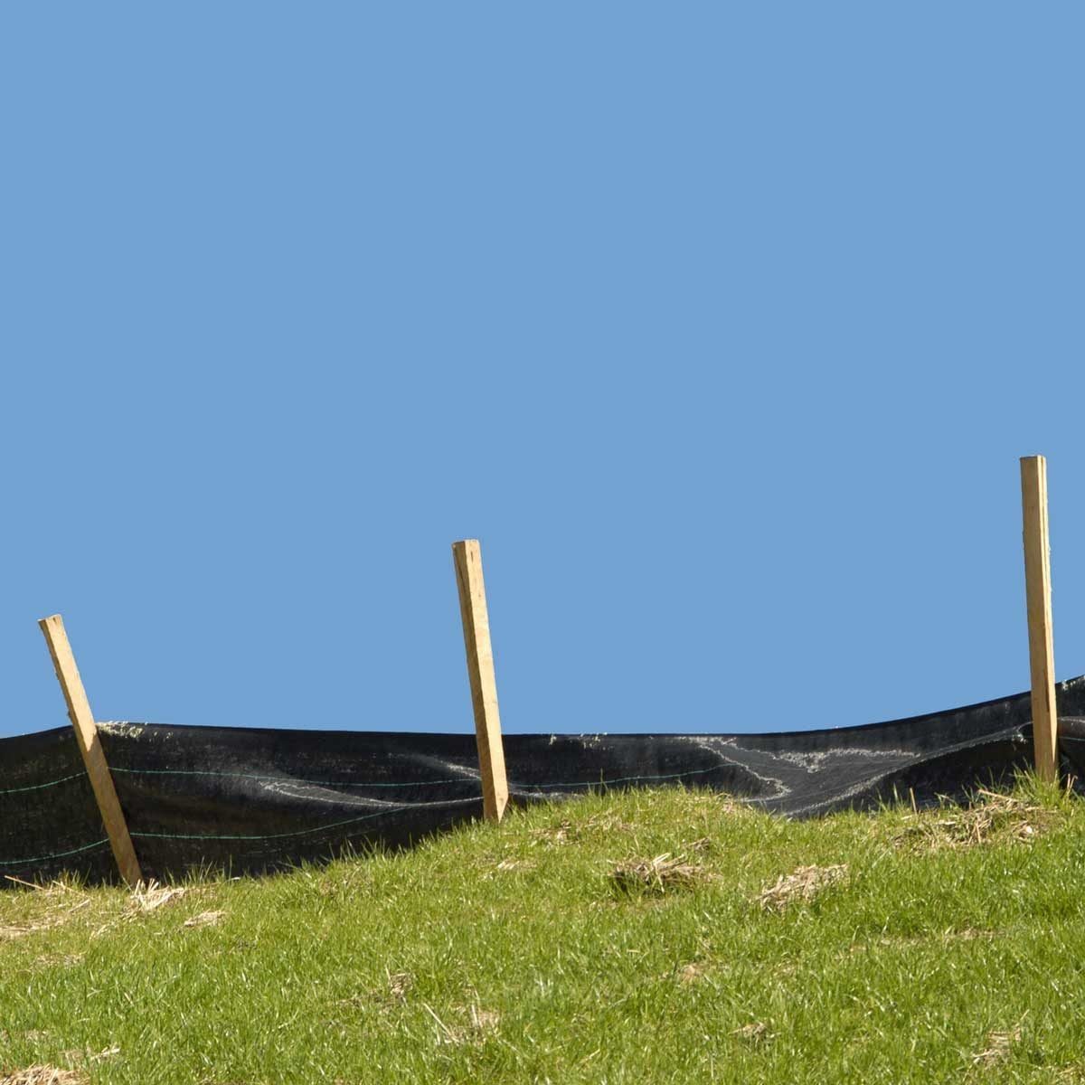 A black barrier rests on green grass, supported by wooden stakes, under a clear blue sky.