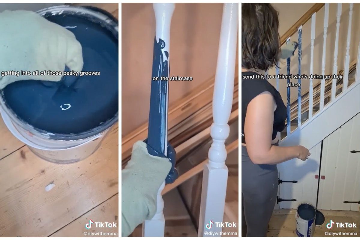 A gloved hand paints a staircase banister with dark blue paint, surrounded by wooden floors and a partially painted wall, suggesting a home