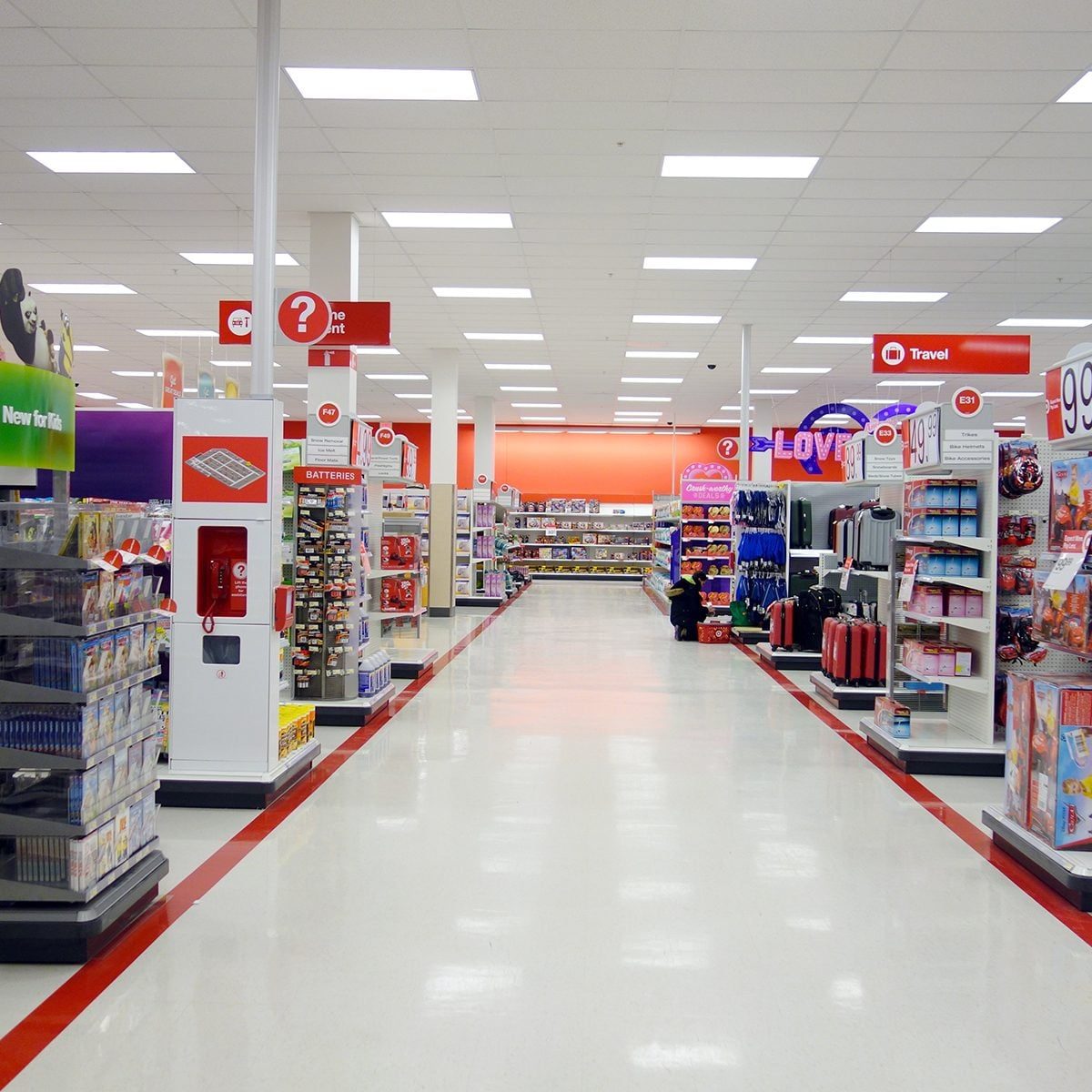 Shelves filled with various products line a brightly lit retail aisle, while clear signage directs shoppers towards different departments li