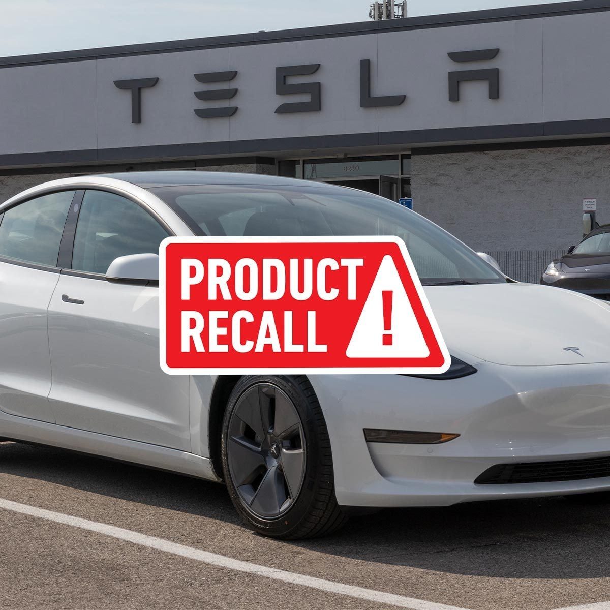 White Tesla vehicle in front of a Tesla dealership with a red "product recall" sticker on top