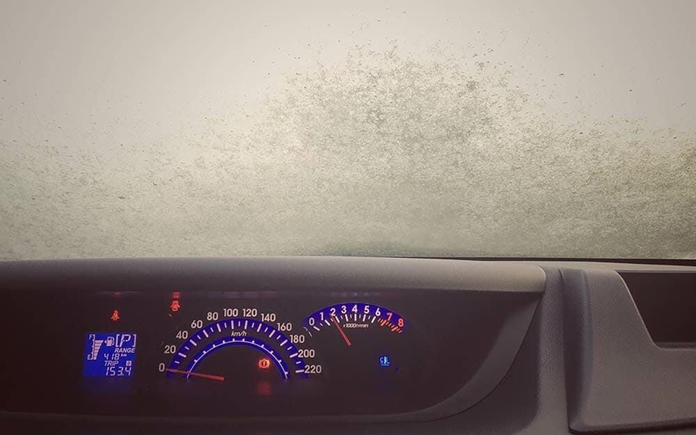 A car dashboard displays gauges and indicators while foggy glass obscures the view outside, suggesting a misty or humid environment.