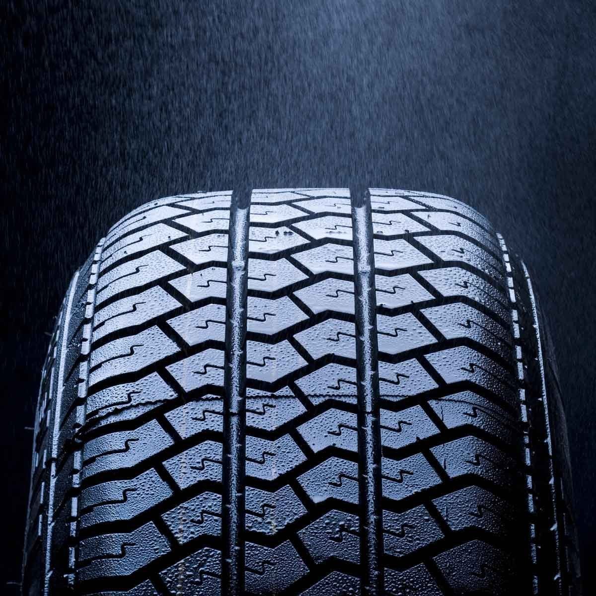 A close-up of a wet tire with a textured surface, illuminated against a dark background, emphasizing its grooves and water droplets.