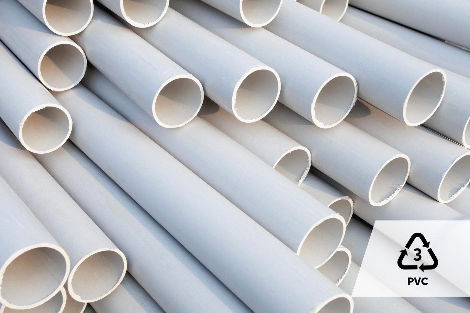 Gray PVC pipes are stacked closely together, showcasing their hollow centers and smooth surfaces, with a recycling symbol for PVC visible in