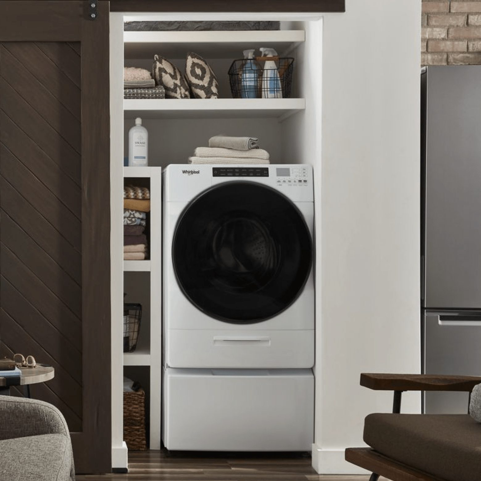 A white washer-dryer sits in an alcove, surrounded by neatly stacked towels and cleaning supplies, in a modern, stylish room.