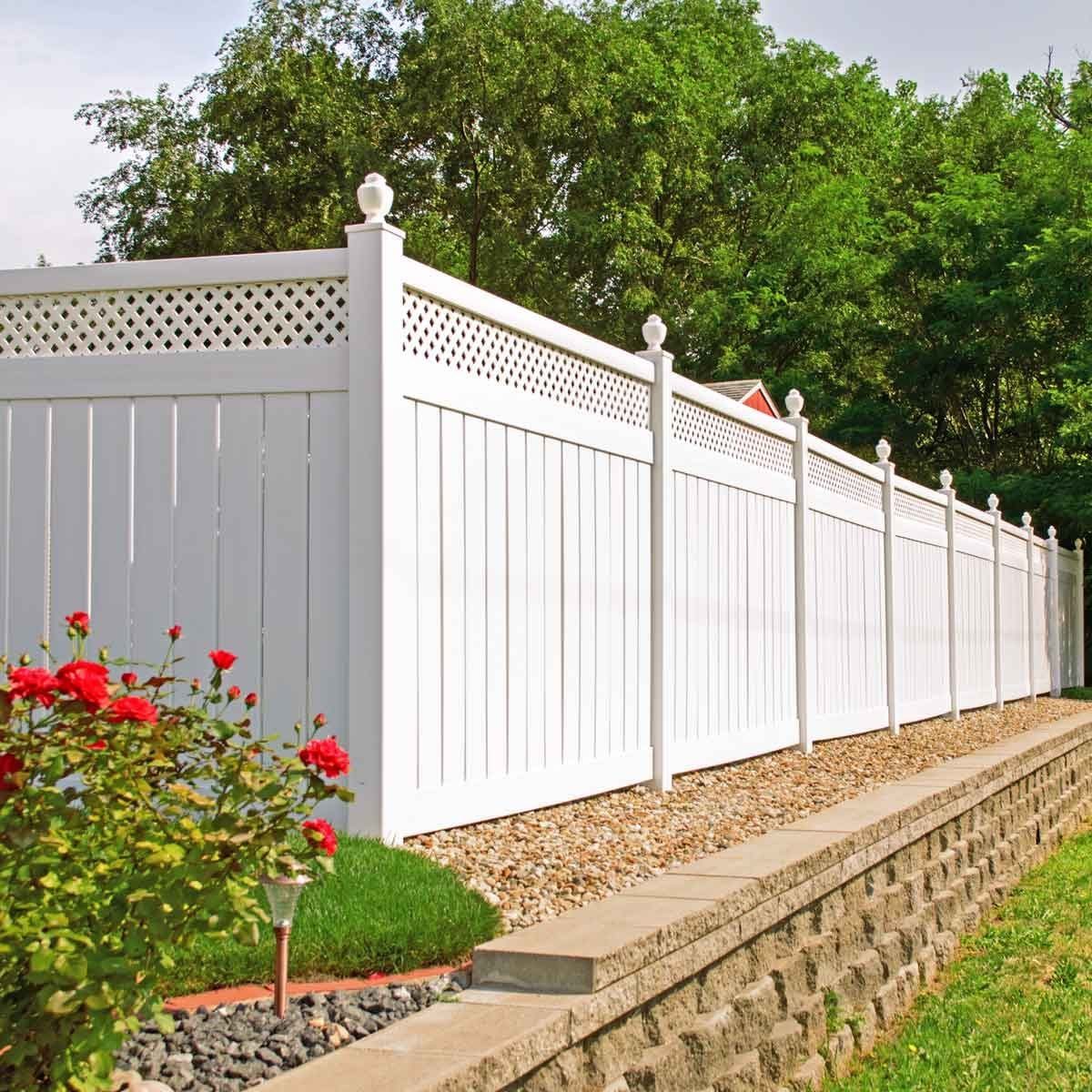 A white wooden fence lines a gravel pathway, bordered by colorful flowers and greenery, creating a tranquil outdoor space in a well-maintain