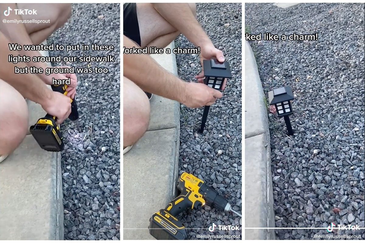 A person uses a drill to install a light in gravel near a sidewalk. The light is placed upright, illuminating the area.